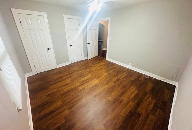 unfurnished bedroom with baseboards, arched walkways, and wood finished floors