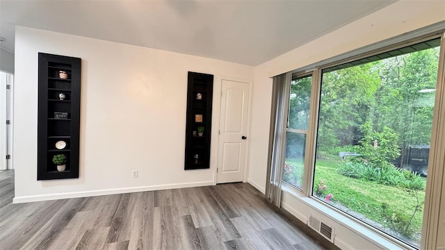 spare room with baseboards, wood finished floors, and visible vents