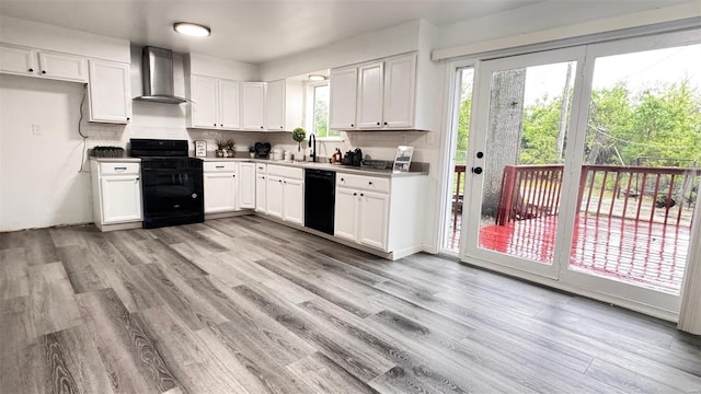 kitchen with wall chimney exhaust hood, white cabinetry, a sink, light wood finished floors, and black appliances