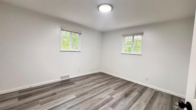 empty room with visible vents, baseboards, a wealth of natural light, and dark wood-style floors