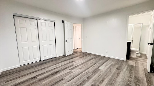unfurnished bedroom with connected bathroom, baseboards, wood finished floors, and a closet