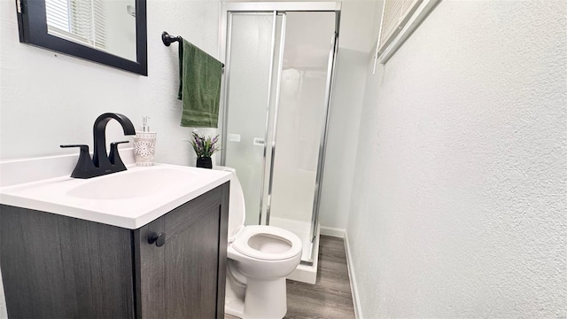 full bathroom featuring a shower stall, wood finished floors, vanity, toilet, and a textured wall