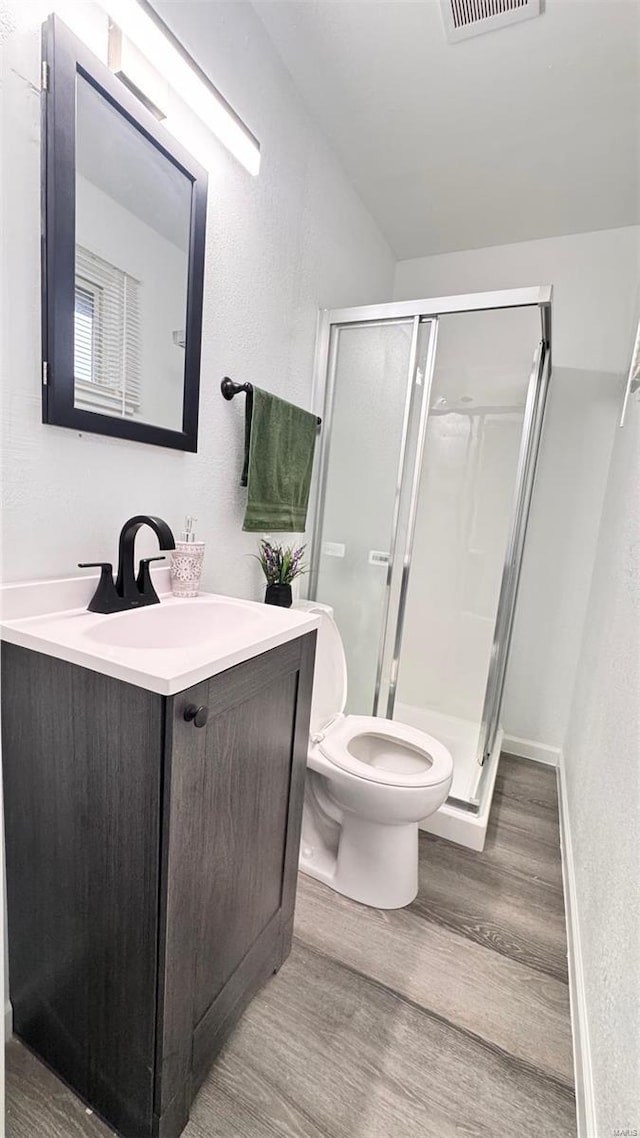 bathroom featuring vanity, toilet, wood finished floors, visible vents, and a stall shower