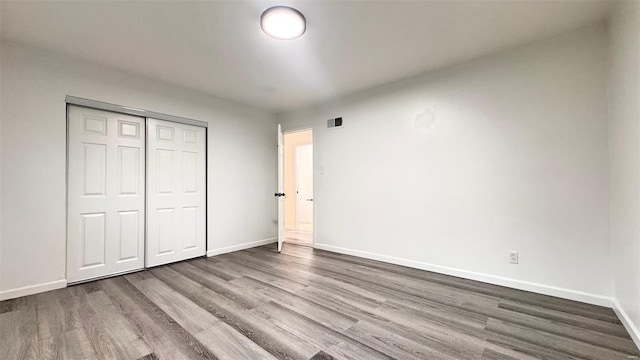 unfurnished bedroom with visible vents, baseboards, wood finished floors, and a closet