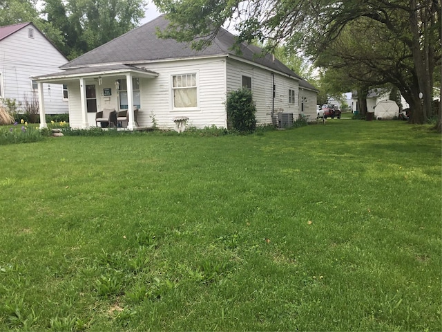 exterior space with roof with shingles, central AC unit, a porch, and a front yard