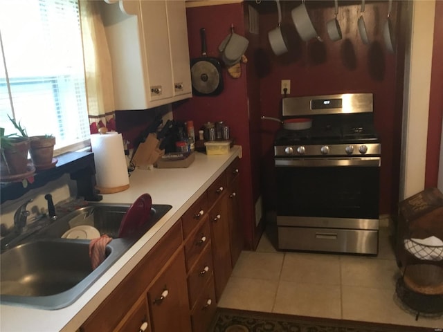 kitchen with light tile patterned flooring, stainless steel gas range oven, light countertops, white cabinetry, and a sink