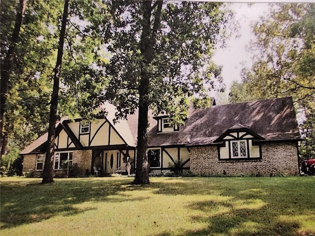 tudor home with brick siding and a front lawn