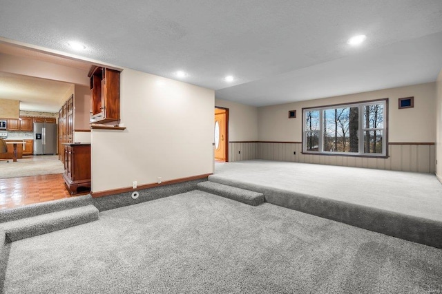 unfurnished living room featuring light colored carpet, recessed lighting, and a wainscoted wall