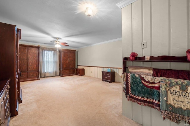 living area featuring crown molding, a ceiling fan, light carpet, and wainscoting