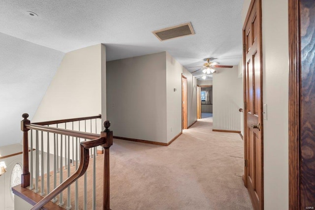 corridor featuring a textured ceiling, visible vents, baseboards, an upstairs landing, and light carpet