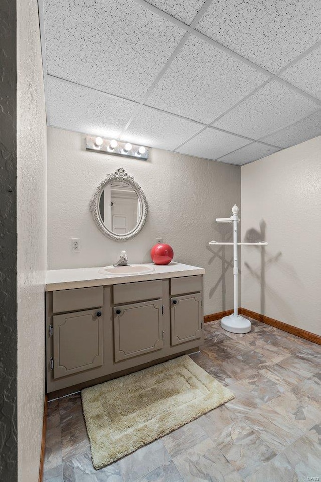 bathroom with vanity, a paneled ceiling, a textured wall, and baseboards