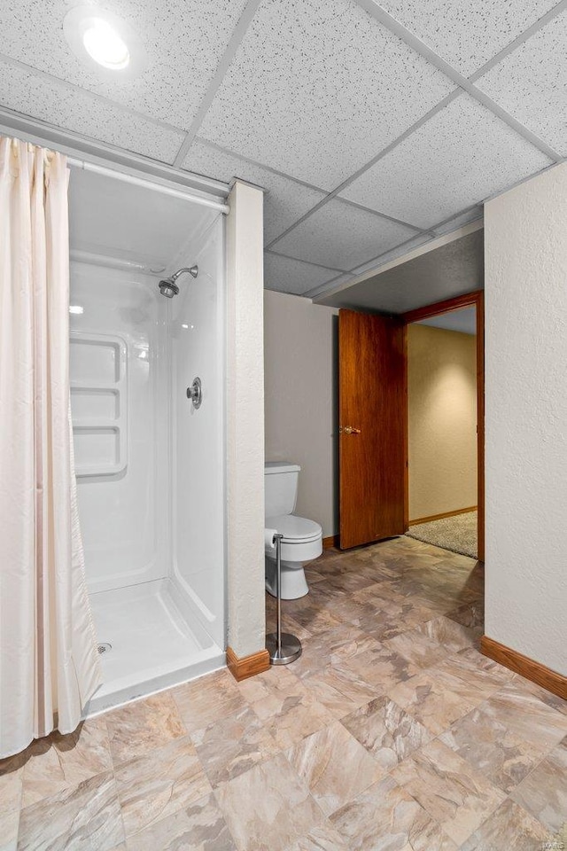 full bath with toilet, baseboards, a drop ceiling, and a stall shower