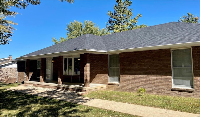 ranch-style house featuring a porch, brick siding, a front yard, and roof with shingles