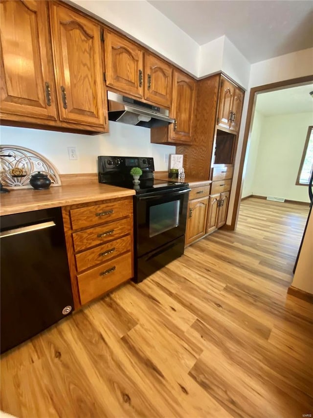kitchen featuring under cabinet range hood, brown cabinetry, light wood finished floors, and black appliances