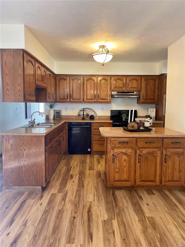 kitchen featuring under cabinet range hood, brown cabinets, a sink, light wood-style flooring, and black appliances