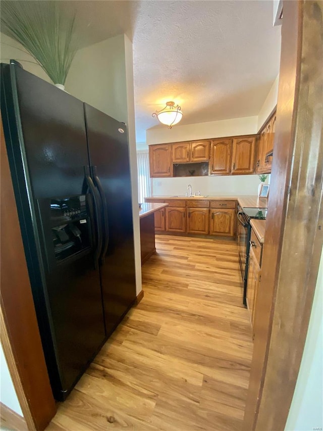 kitchen featuring light wood-type flooring, brown cabinetry, a sink, and black appliances