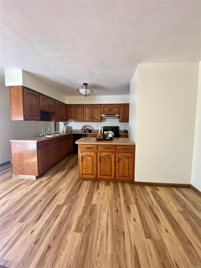 kitchen featuring a sink, a peninsula, exhaust hood, and light countertops