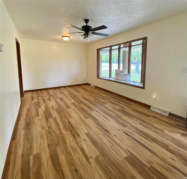 empty room with ceiling fan, light wood finished floors, a textured ceiling, baseboards, and visible vents