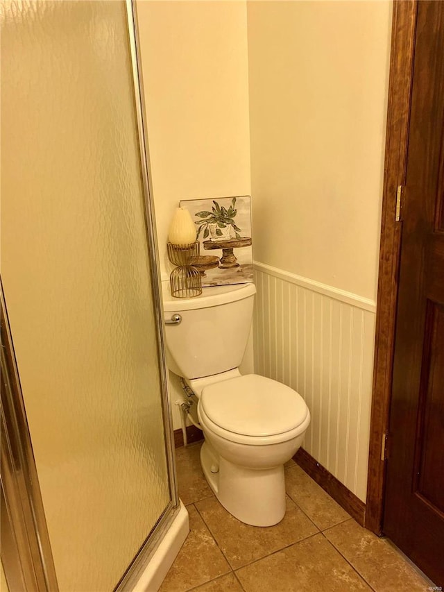 bathroom with wainscoting, toilet, tile patterned floors, baseboards, and a shower stall
