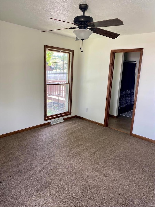 empty room featuring ceiling fan, a textured ceiling, dark carpet, baseboards, and visible vents