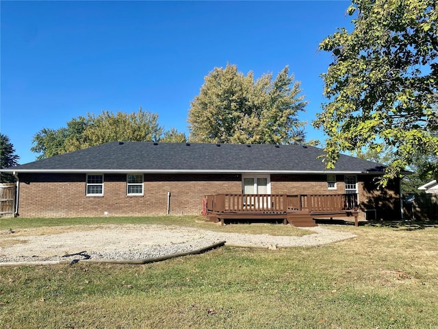 back of property with a lawn, brick siding, a wooden deck, and roof with shingles