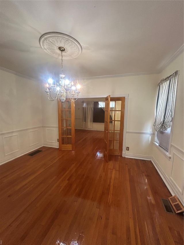 unfurnished dining area with an inviting chandelier, ornamental molding, a decorative wall, and hardwood / wood-style floors