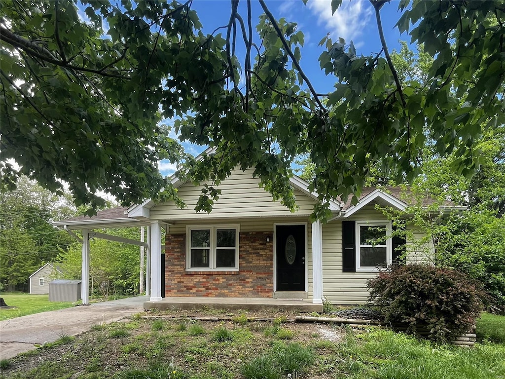 bungalow-style house featuring an outdoor structure, an attached carport, driveway, and brick siding