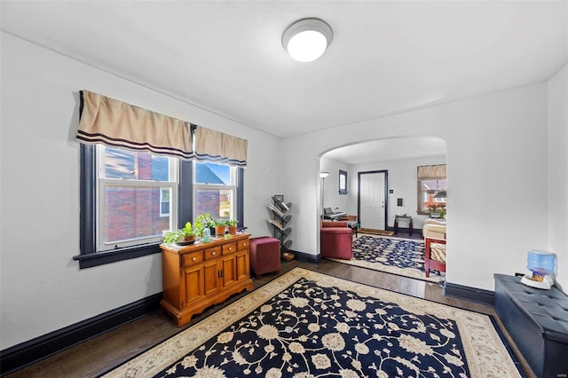 corridor with arched walkways, baseboards, plenty of natural light, and wood finished floors
