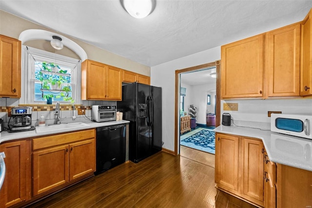 kitchen with a sink, light countertops, dark wood-type flooring, backsplash, and black appliances
