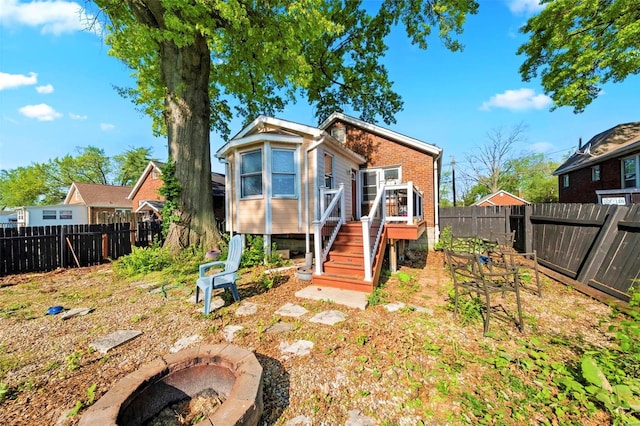 rear view of house with brick siding, a fire pit, a fenced backyard, and a wooden deck