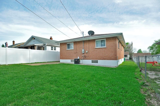back of house with a fenced backyard, central AC unit, a yard, and brick siding
