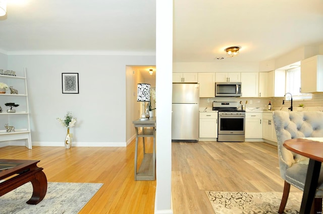 kitchen featuring decorative backsplash, light countertops, white cabinetry, light wood-style flooring, and appliances with stainless steel finishes