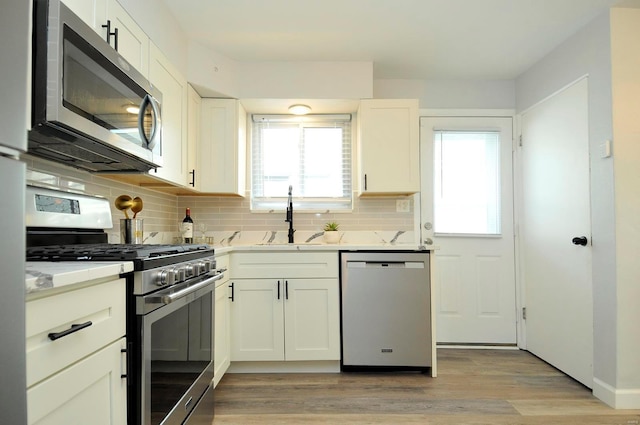 kitchen with a sink, appliances with stainless steel finishes, white cabinets, and tasteful backsplash