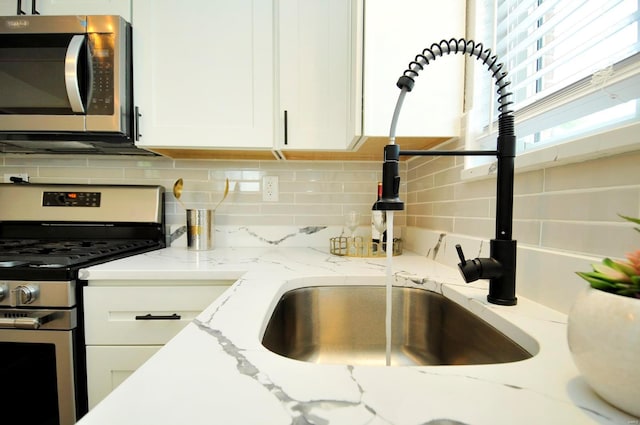 kitchen with backsplash, light stone countertops, a sink, white cabinets, and stainless steel appliances