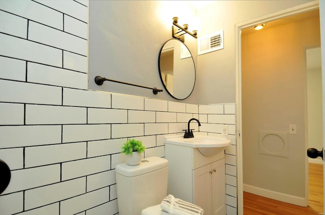 bathroom featuring vanity, toilet, tile walls, wood finished floors, and visible vents