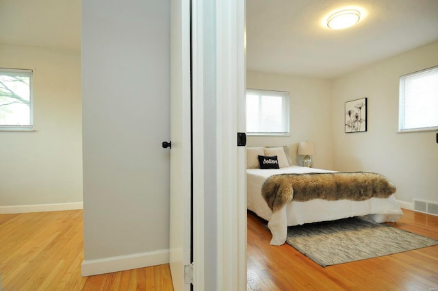 bedroom featuring baseboards, multiple windows, wood finished floors, and visible vents