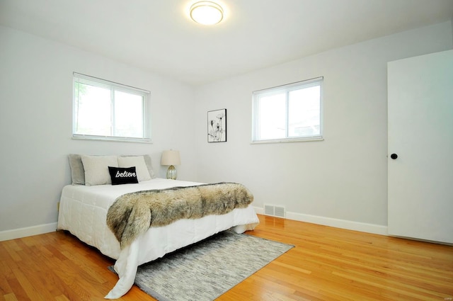 bedroom featuring light wood-style floors, baseboards, multiple windows, and visible vents