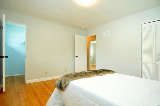 bedroom featuring a closet, baseboards, wood finished floors, and visible vents