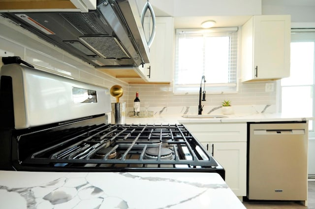 kitchen with white cabinets, light stone countertops, a sink, stainless steel appliances, and tasteful backsplash