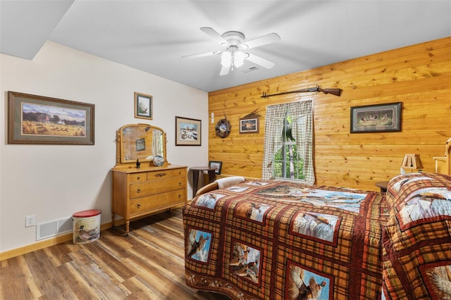 bedroom featuring a ceiling fan, baseboards, visible vents, wood walls, and wood finished floors