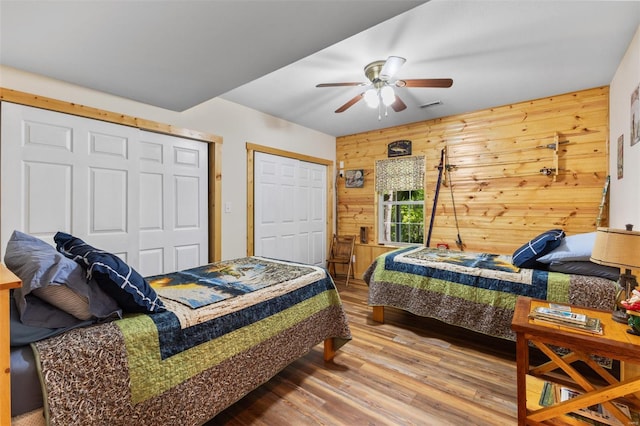bedroom with wood walls, a ceiling fan, visible vents, and wood finished floors