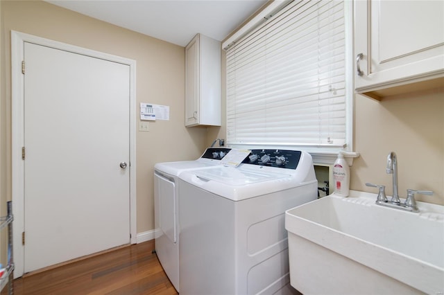 laundry room with cabinet space, washer and clothes dryer, a sink, and wood finished floors