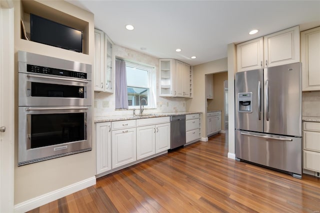 kitchen featuring light wood-style floors, baseboards, a sink, backsplash, and stainless steel appliances