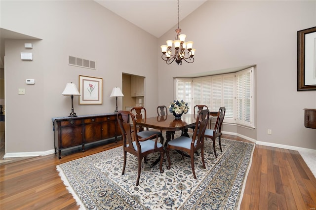 dining room featuring visible vents, wood finished floors, high vaulted ceiling, baseboards, and a chandelier
