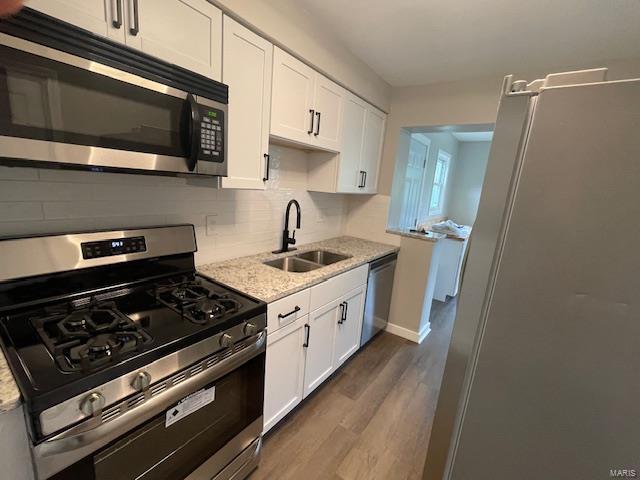 kitchen with light stone counters, appliances with stainless steel finishes, a sink, white cabinetry, and dark wood-type flooring