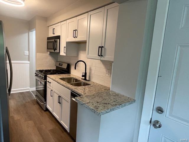 kitchen with light stone countertops, dark wood finished floors, a sink, stainless steel appliances, and white cabinetry