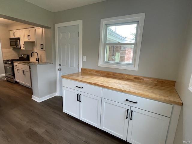 kitchen with dark wood-type flooring, a sink, white cabinetry, and stainless steel gas range oven