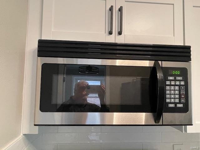 interior details with white cabinets, stainless steel microwave, and backsplash