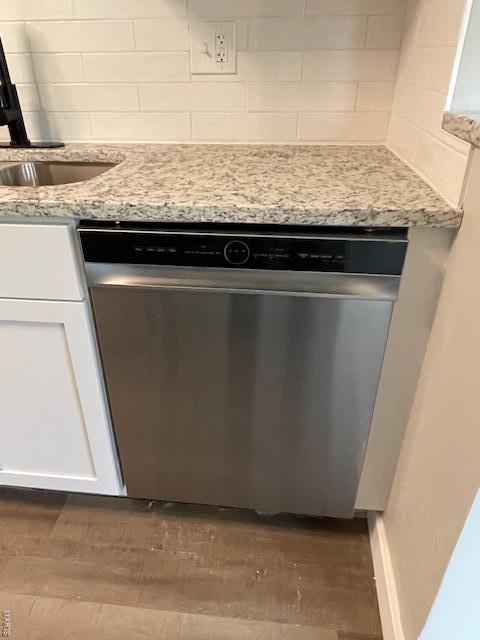 interior details with stainless steel dishwasher, dark wood-style floors, white cabinetry, a sink, and backsplash