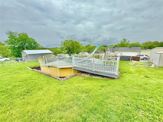 pool featuring a lawn, a water slide, an outbuilding, and a deck
